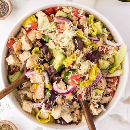 Two salad spoons mix a bowl of Italian chopped salad.