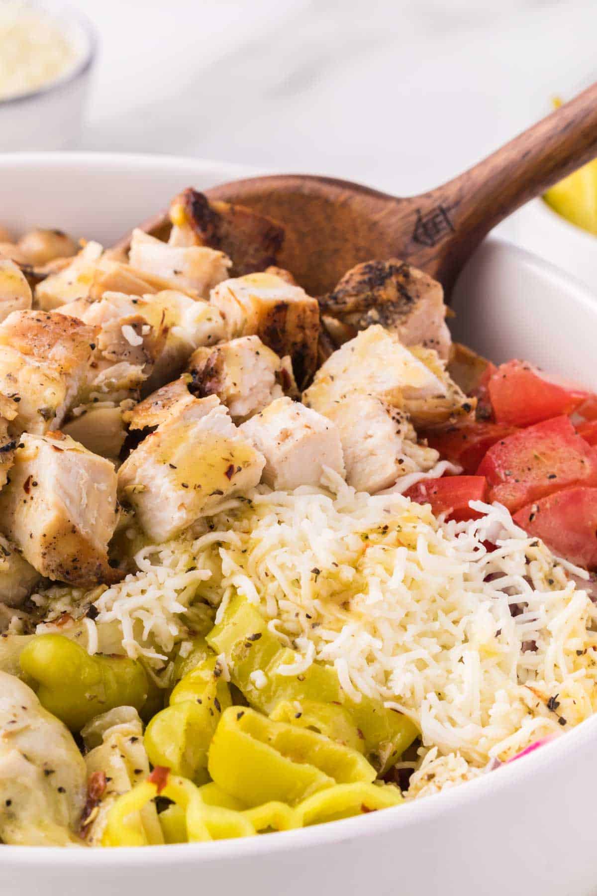 A spoon stirs a big bowl of Italian chopped salad.