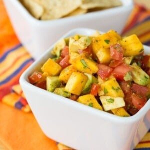 A square white bowl is full of colorful mango avocado salsa.