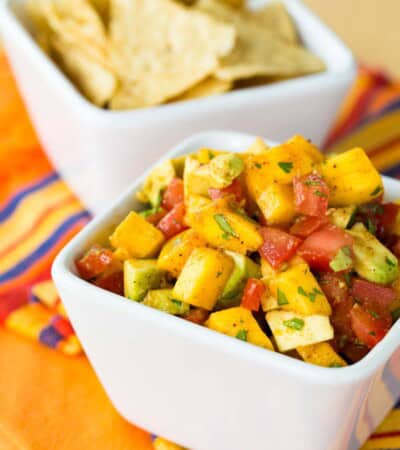 A square white bowl is full of colorful mango avocado salsa.