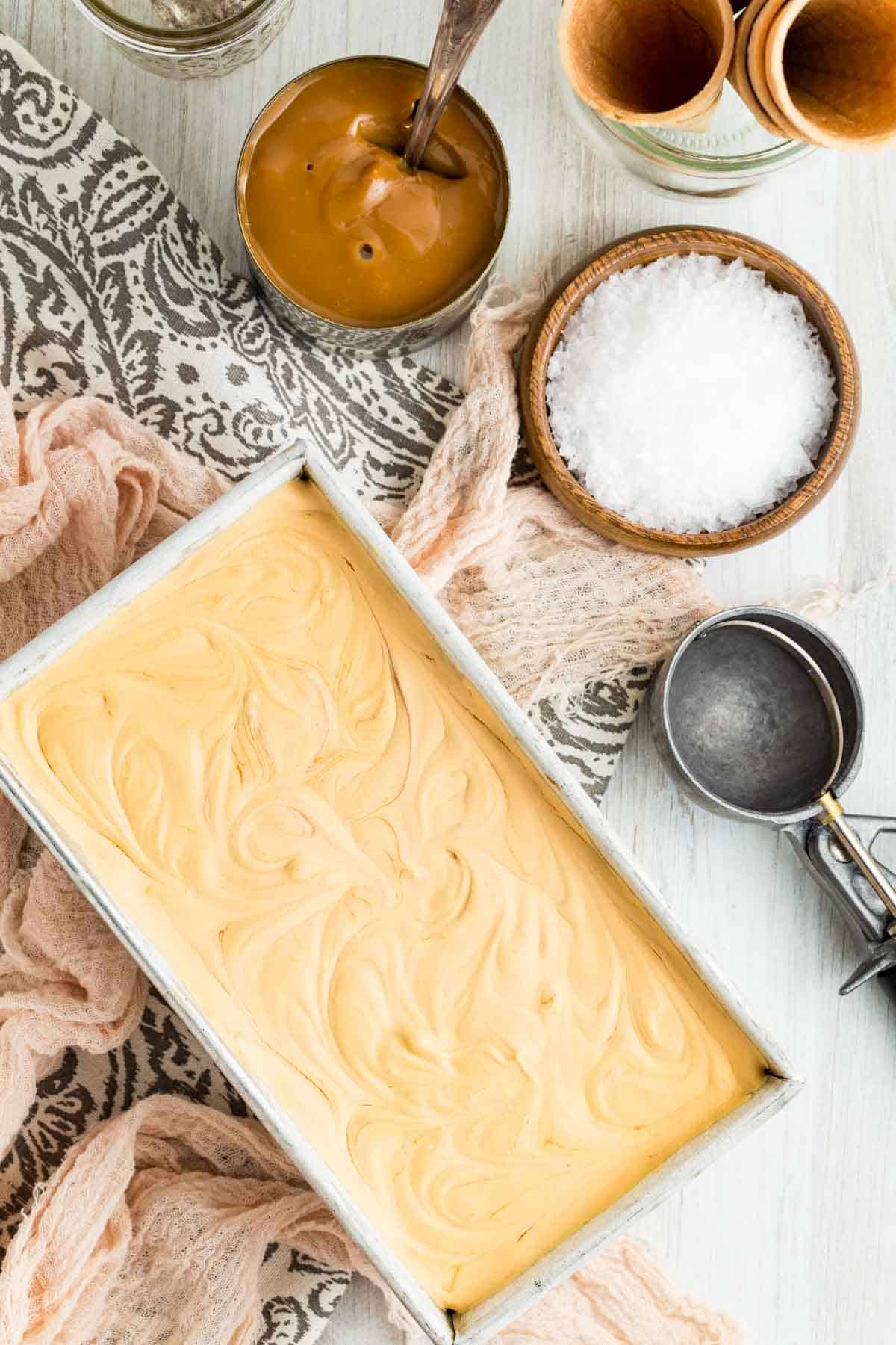 A metal loaf pan is filled with dulce de leche ice cream with salt and dulce de leche next to it.