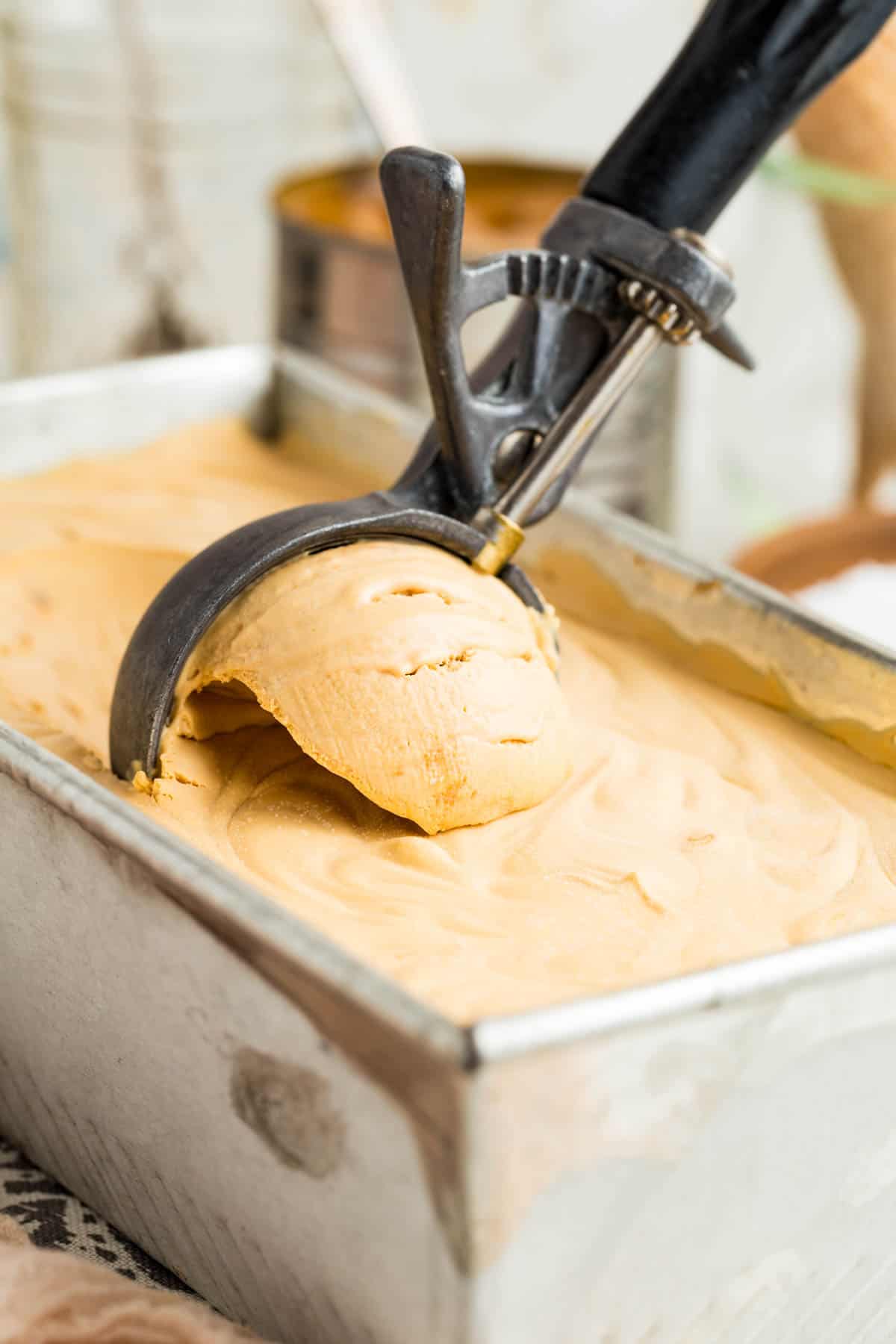 An ice cream scoop digs into a metal loaf pan of dulce de leche ice cream.