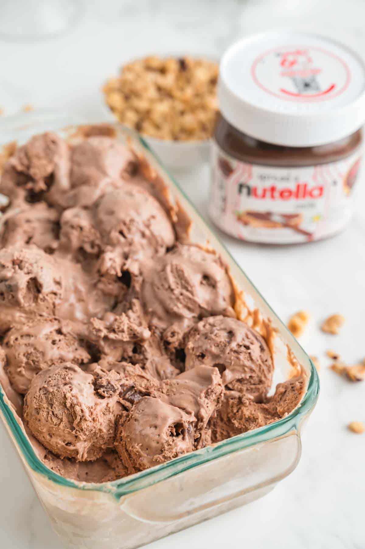 A loaf pan holds nutella ice cream with a jar of nutella in the background.