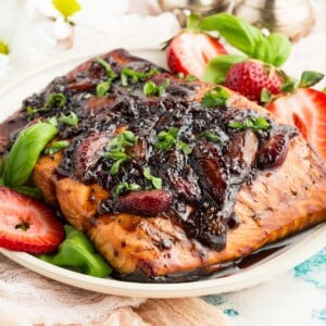 A piece of salmon on a plate topped with a strawberry balsamic glaze.