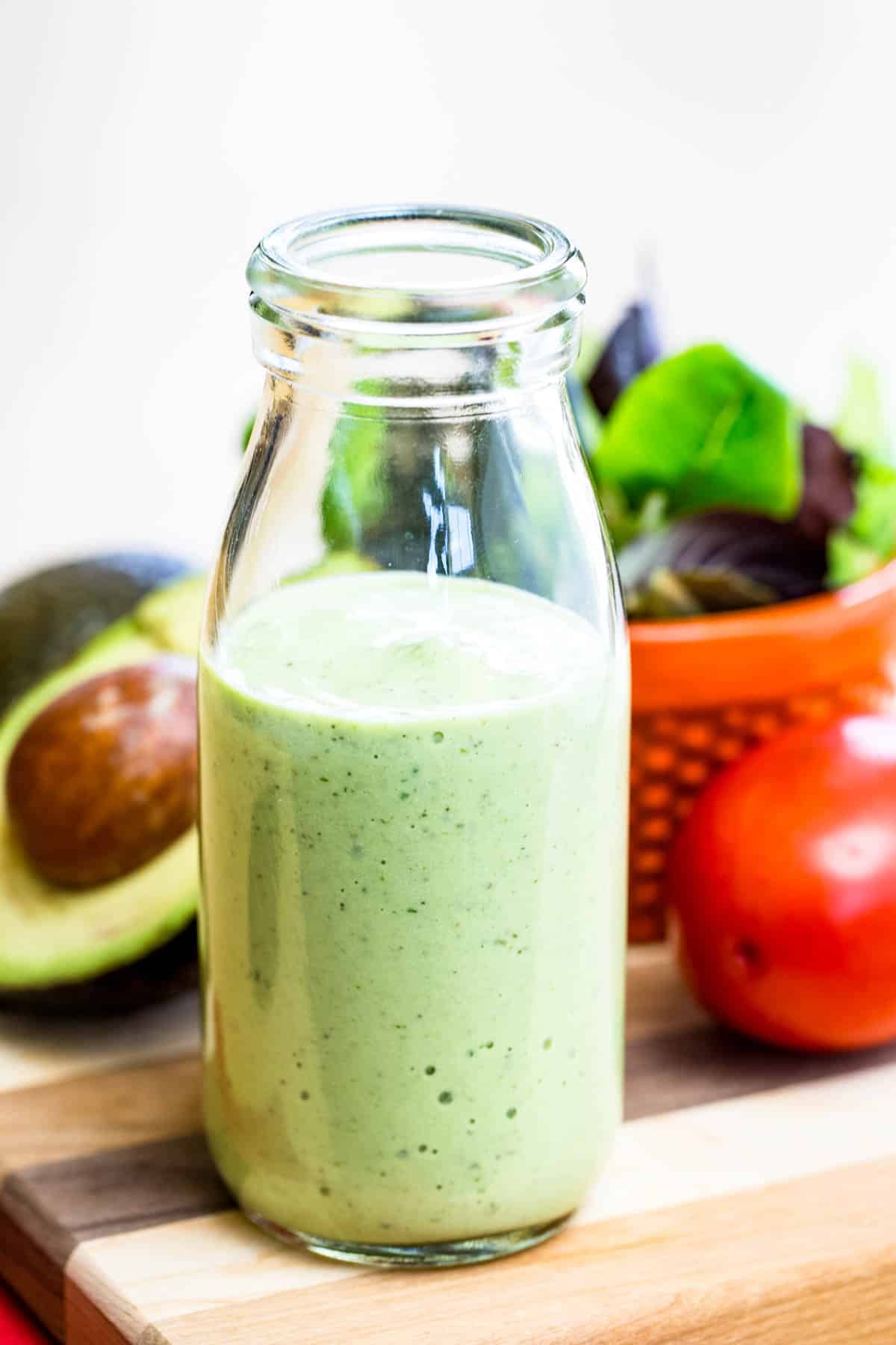 A glass bottle of avocado ranch dressing on a wooden board.