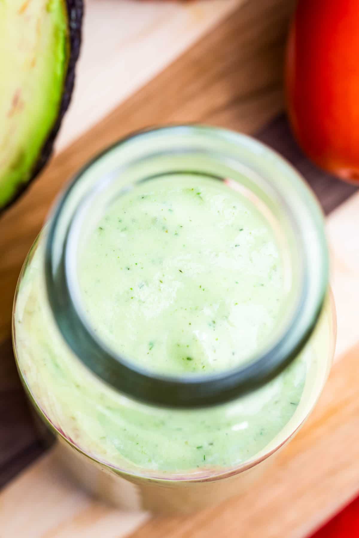 Avocado ranch dressing is seen through the round opening of a glass bottle.