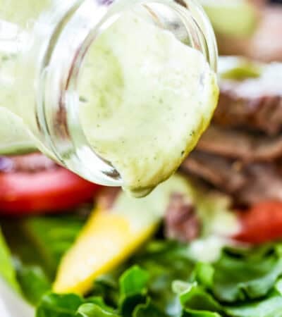 Avocado ranch dressing is poured from a bottle onto a salad.