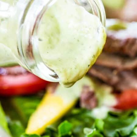 Avocado ranch dressing is poured from a bottle onto a salad.