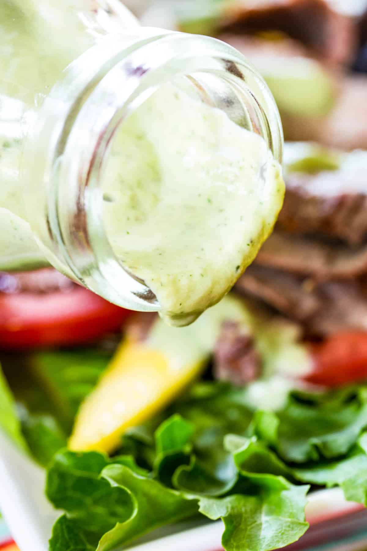 Avocado ranch dressing is poured from a bottle onto a salad.