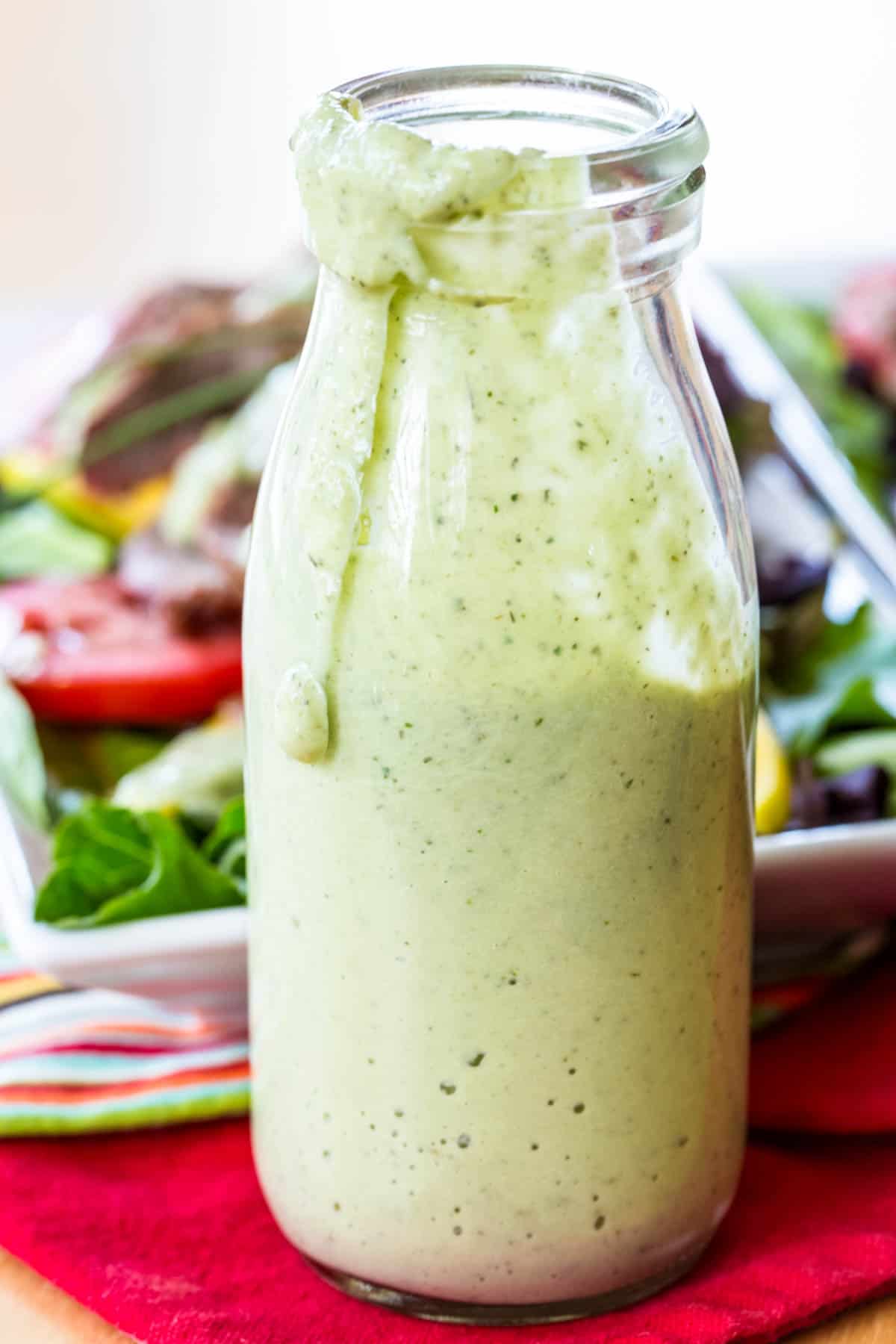 Avocado ranch dressing drips down the side of a glass bottle of dressing.