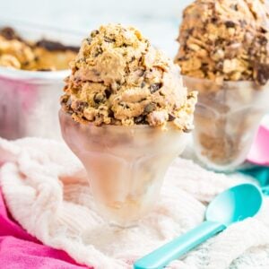 Two glass sundae dishes of dulce de leche fudge ripple ice cream on top of pink and turquoise cloth napkins with a plastic spoon next to it.