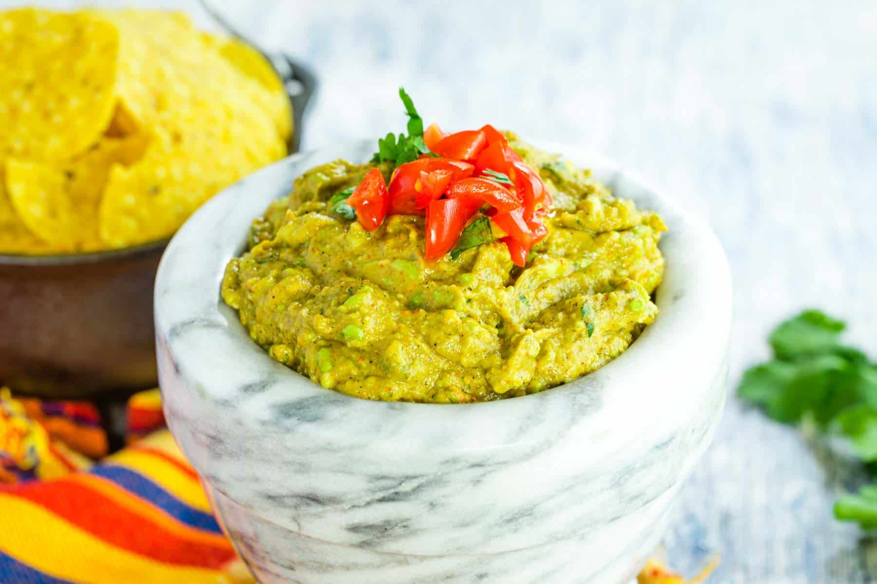 A bowl of easy guacamole is topped with chopped tomatoes.