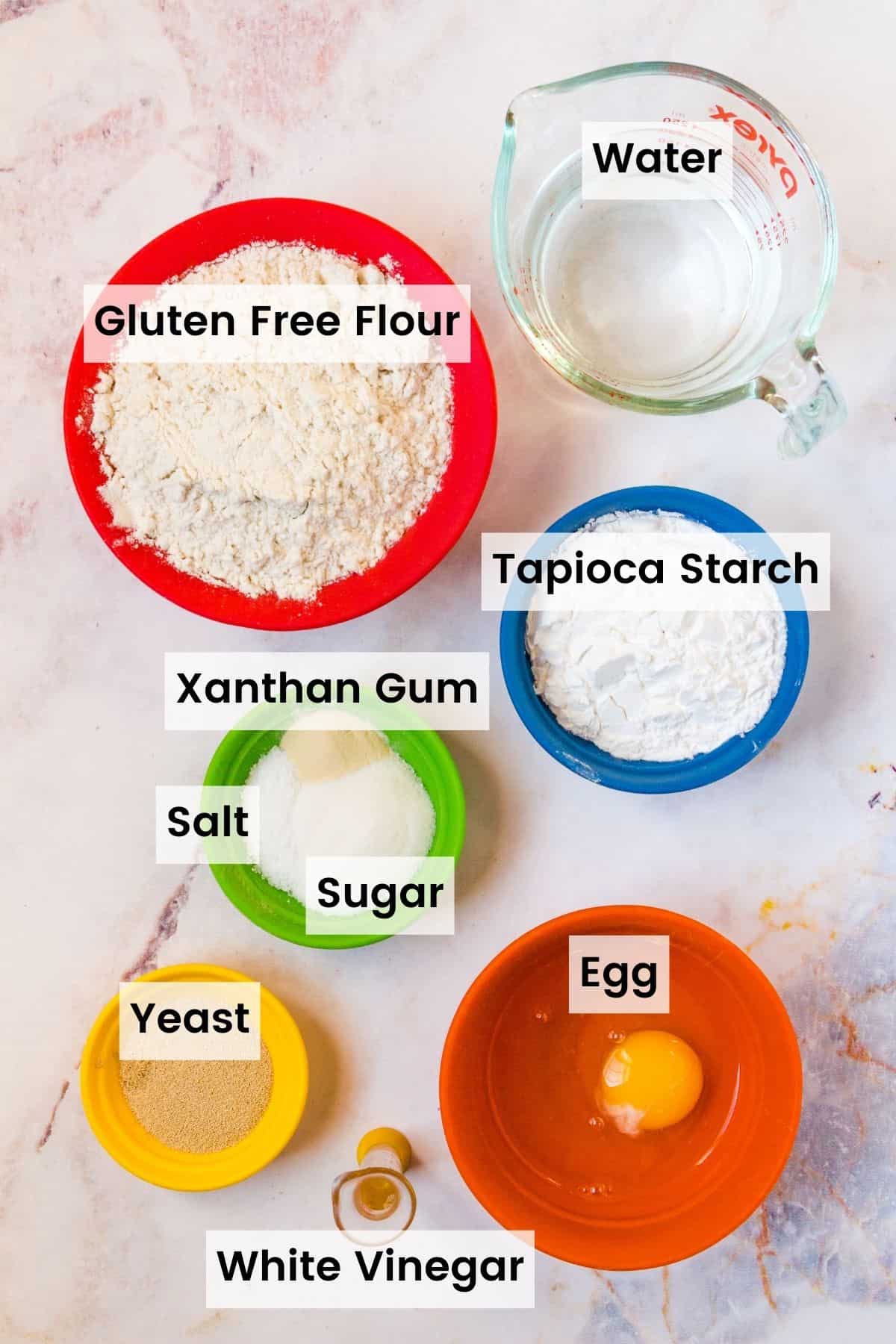 The ingredients for a gluten free French baguette with text labels including Gluten Free Flour, Water, Tapioca Starch, Xanthan Gum, Salt, Sugar, Egg, and White Vinegar.