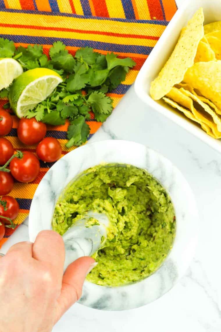 A hand uses a pestle to blend easy guacamole.