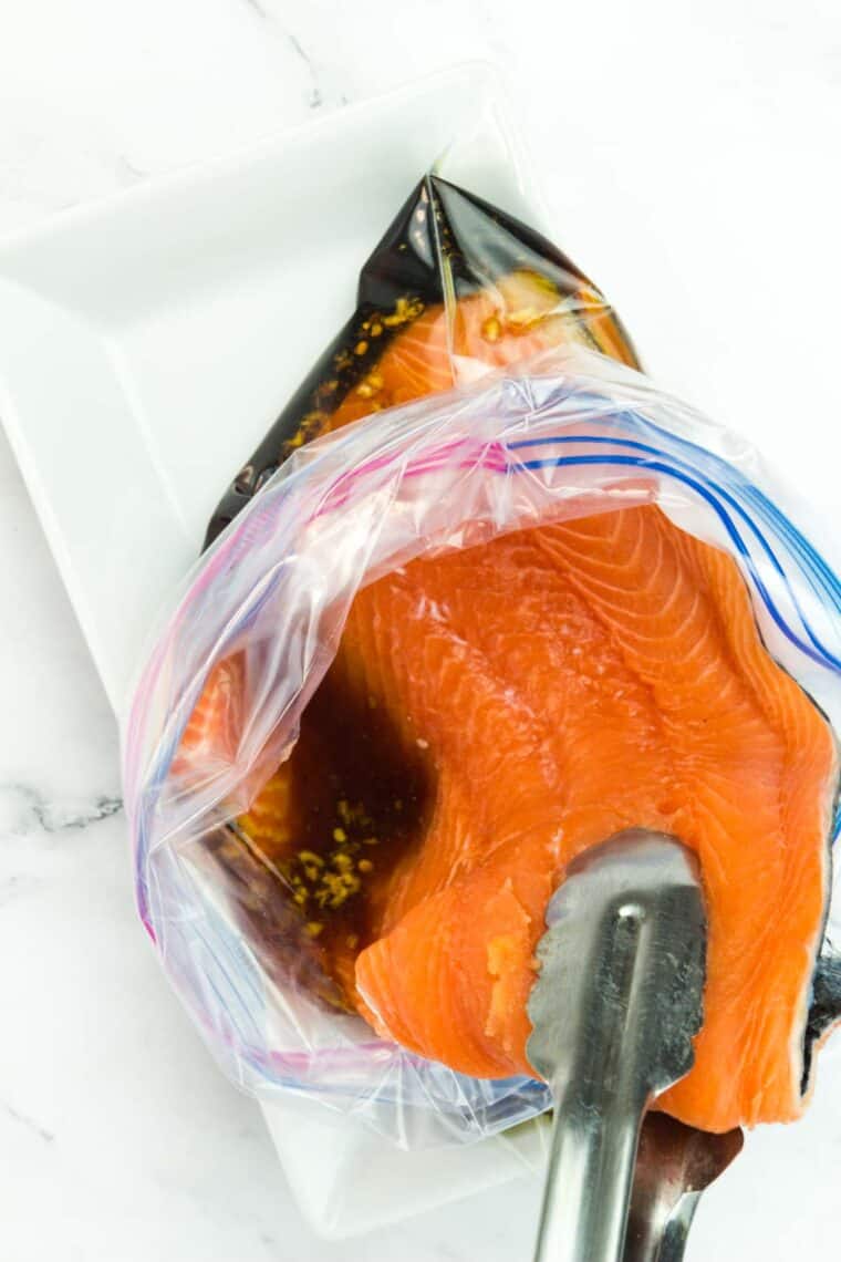 Tongs placing salmon in a plastic bag filled with marinade.