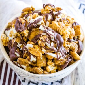 A bowl of a peanut butter-coated snack mix drizzled with white and dark chocolate.