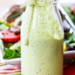 A light green creamy dressing in a glass bottle with a little dripping over the edge with text overlay that says "Avocado Ranch Dressing".