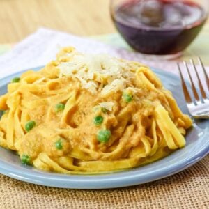 Peas peek out of a plate of pumpkin alfredo noodles.