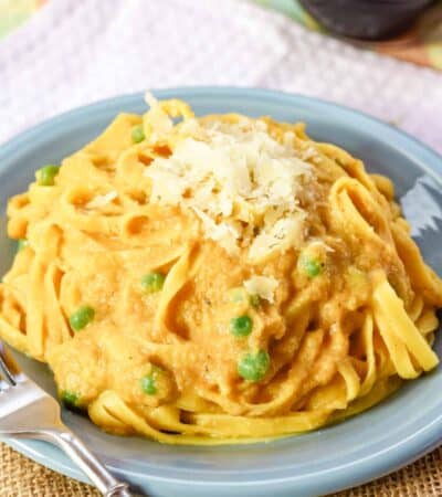 Peas peek out of a plate of pumpkin alfredo noodles.