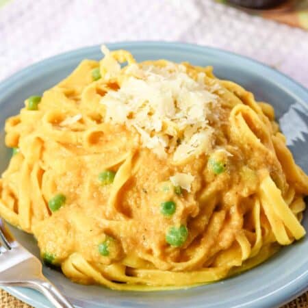 Peas peek out of a plate of pumpkin alfredo noodles.