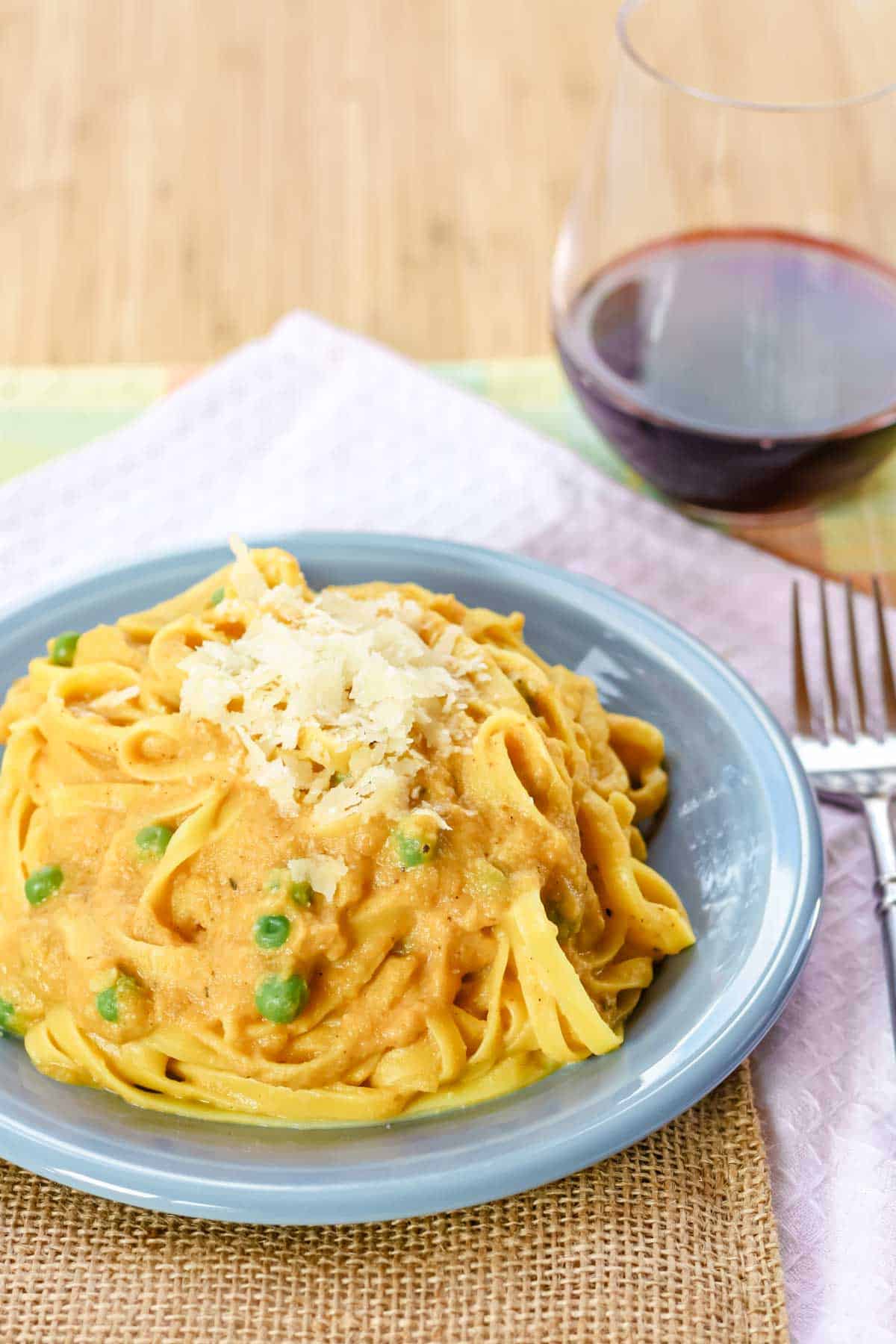 A glass of red and a plate of pumpkin fettuccine alfredo topped with cheese.