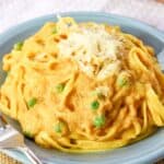 A plate of pasta with a pale orange cream sauce and peas with text overlay that says "Fettuccine Pumpkin Alfredo".