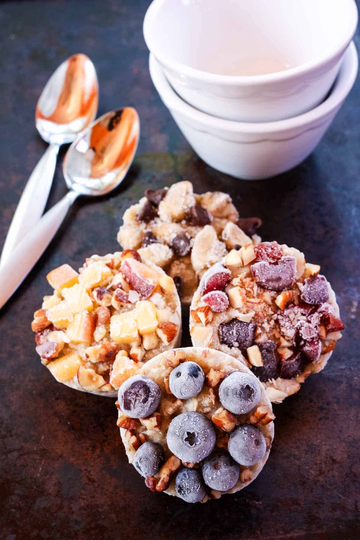 Berries top frozen oatmeal cups with bowls and spoons nearby.