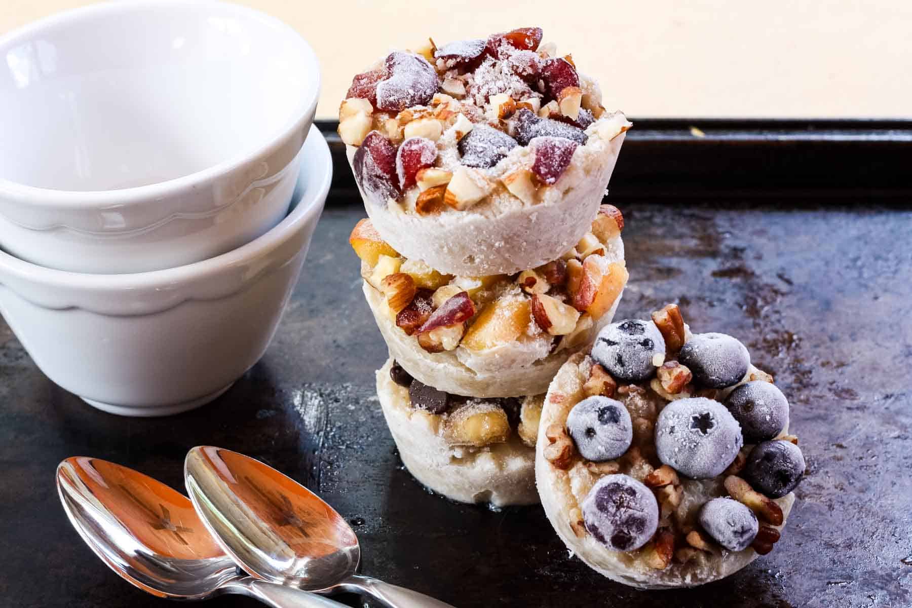 A stack of fruit-topped frozen oatmeal cups with bowls and spoons.