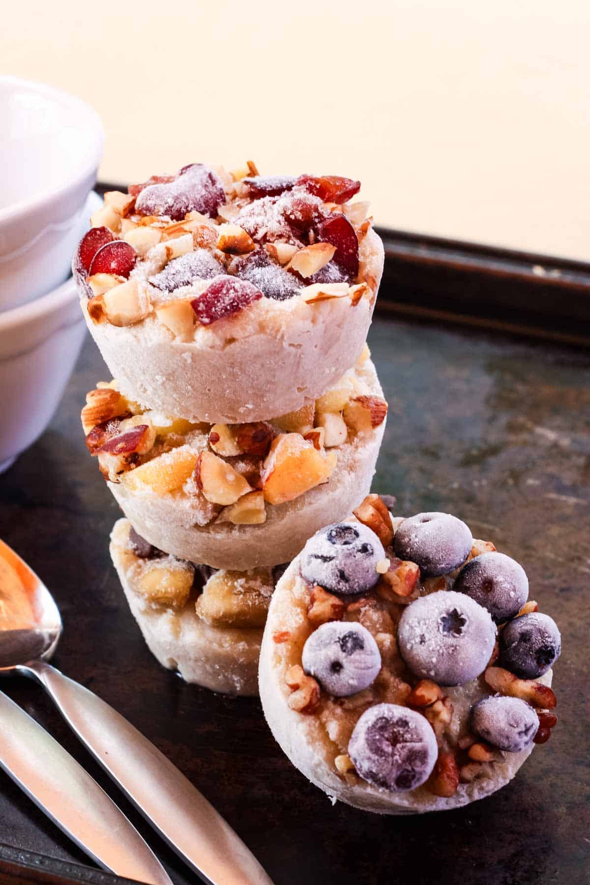 A stack of frozen oatmeal cups that are topped with fruit including blueberries.