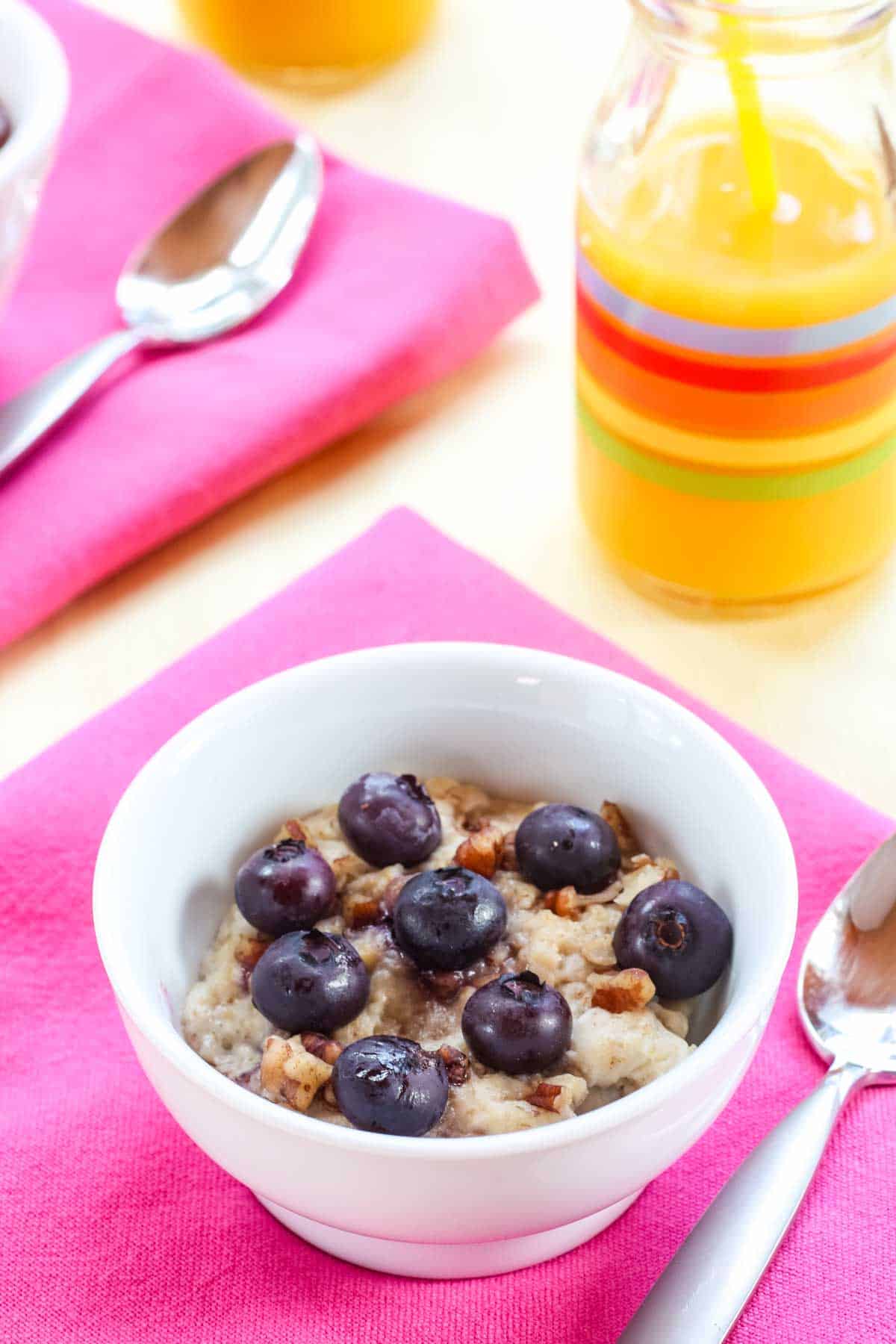 Berries and nuts on top of a bowl of oatmeal with a glass of orange juice.