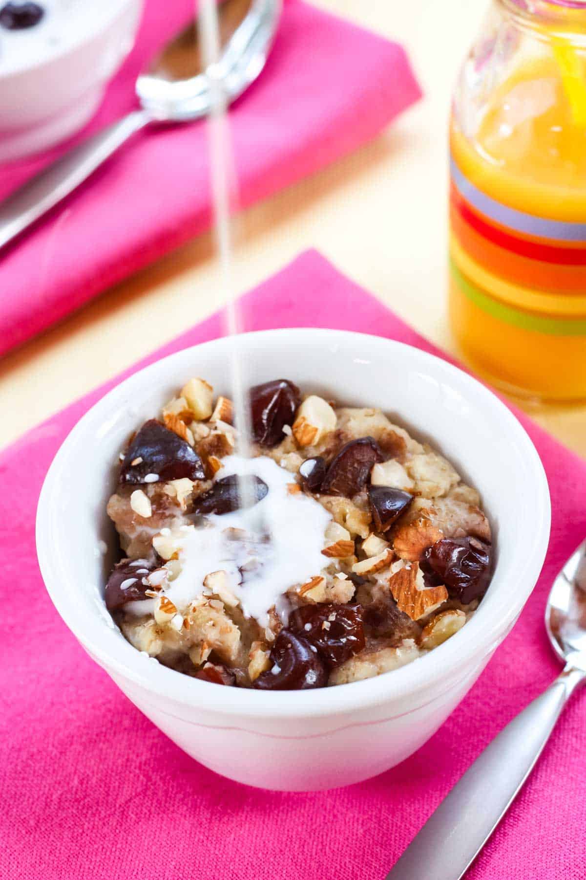 Milk is poured into a bowl of oatmeal with blueberries.