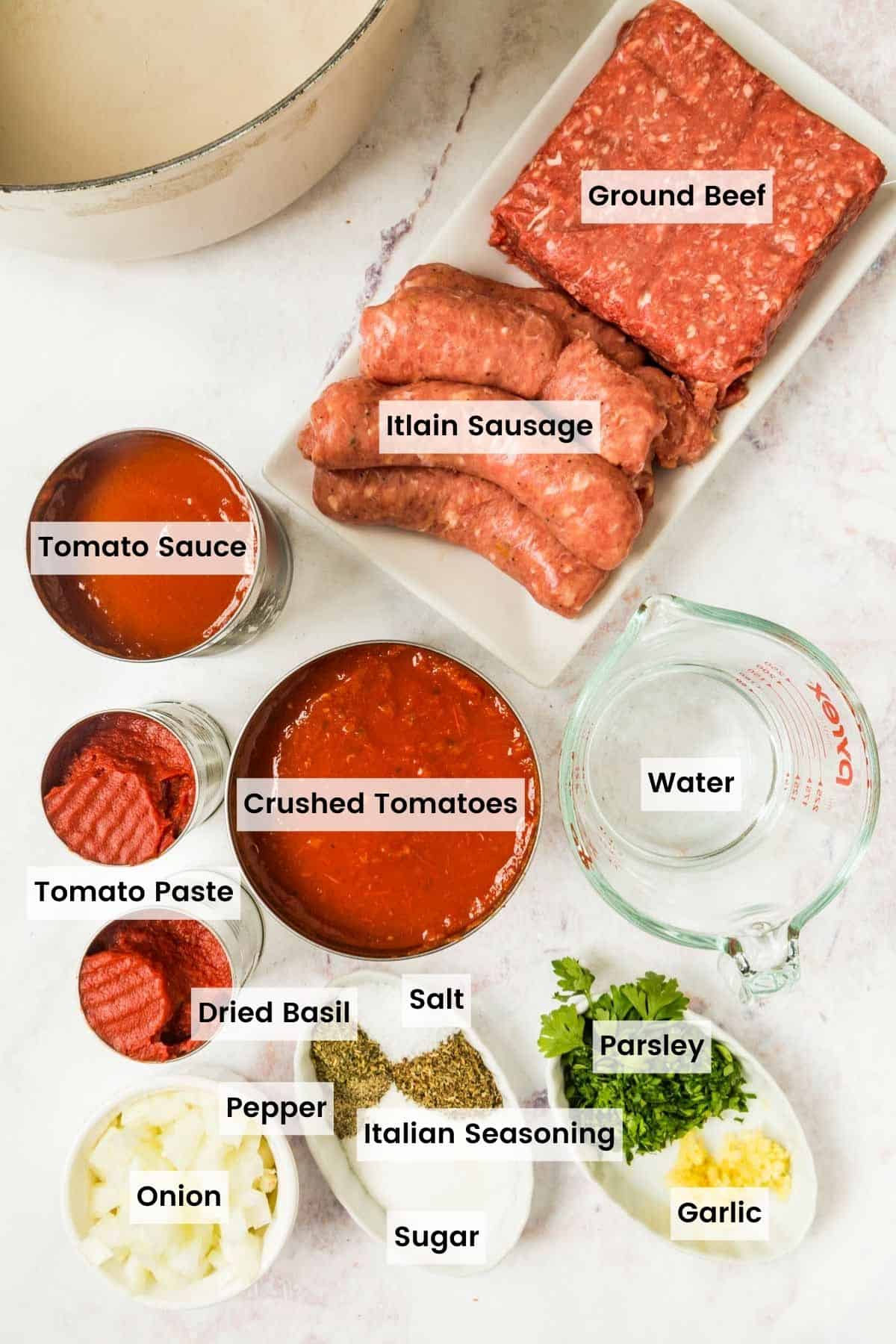 All of the ingredients to make meat sauce for lasagna in bowls, dishes, and cans on a marble countertop with text labels.