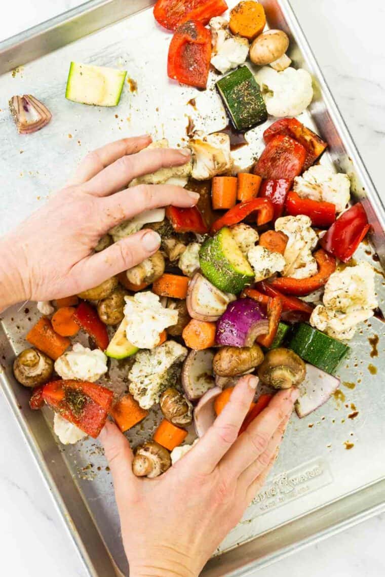 Using hands to toss vegetables on a sheet pan.