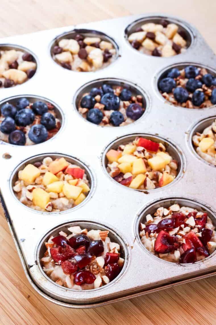 A muffin tin is filled with oatmeal and toppings for frozen oatmeal cups.