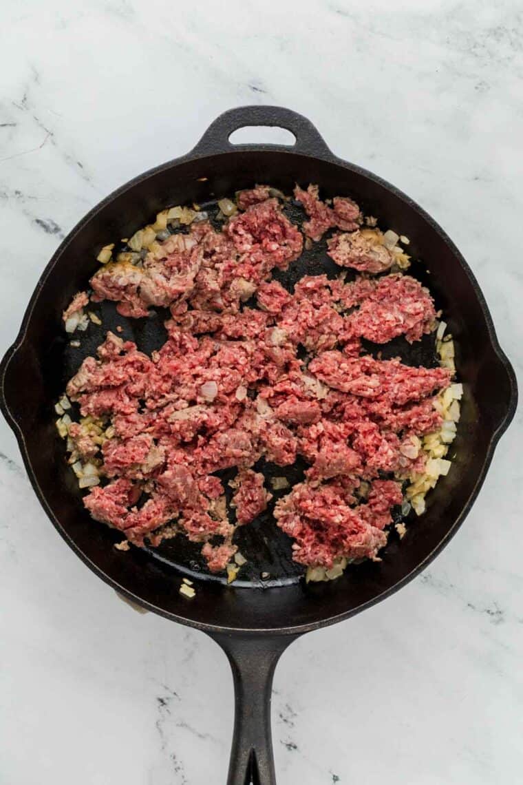 Ground beef is browned in a cast iron pan.