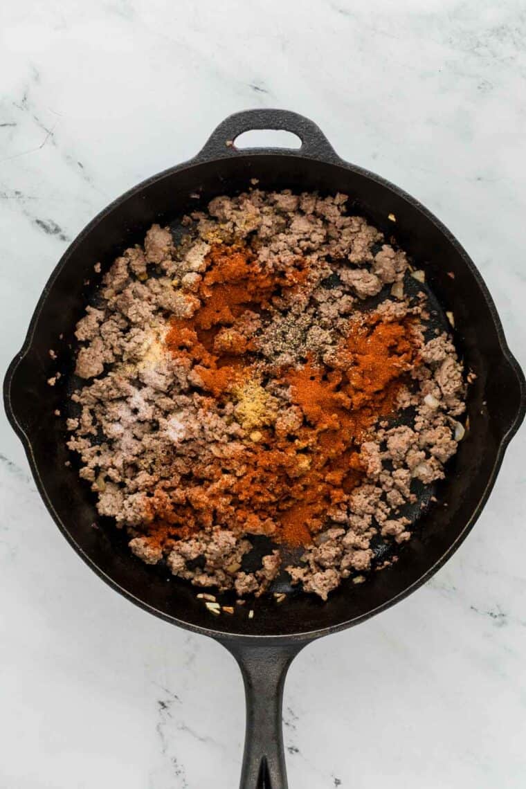 Seasonings are added to ground beef in a cast iron pan.