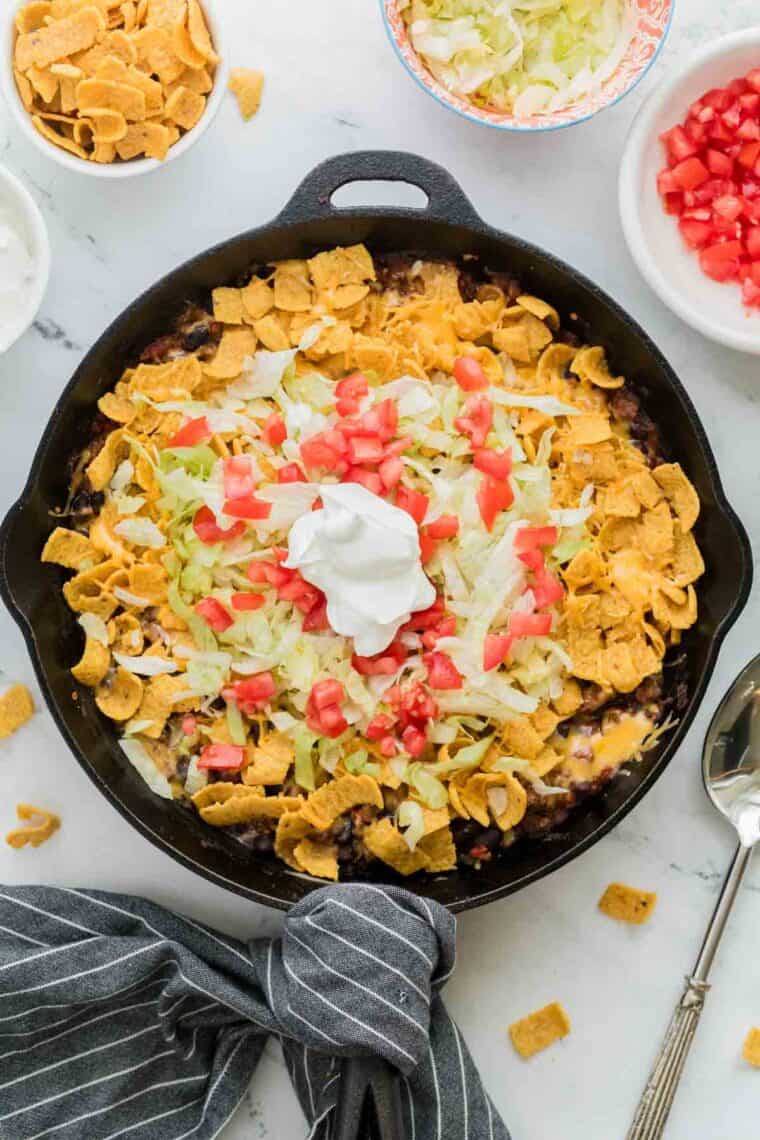 A cast iron pan of walking taco casserole topped with sour cream.