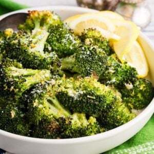 A bowl of roasted broccoli with lemon wedges.