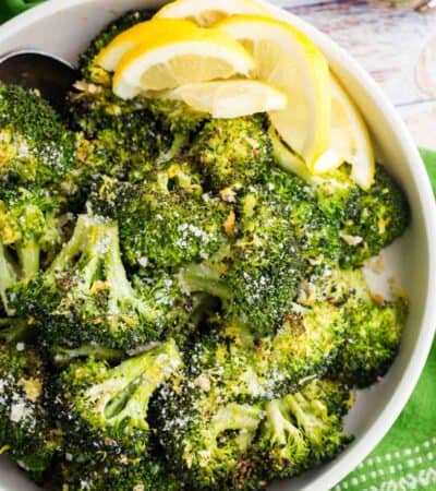 Lemon wedges are served alongside parmesan roasted broccoli in a bowl.