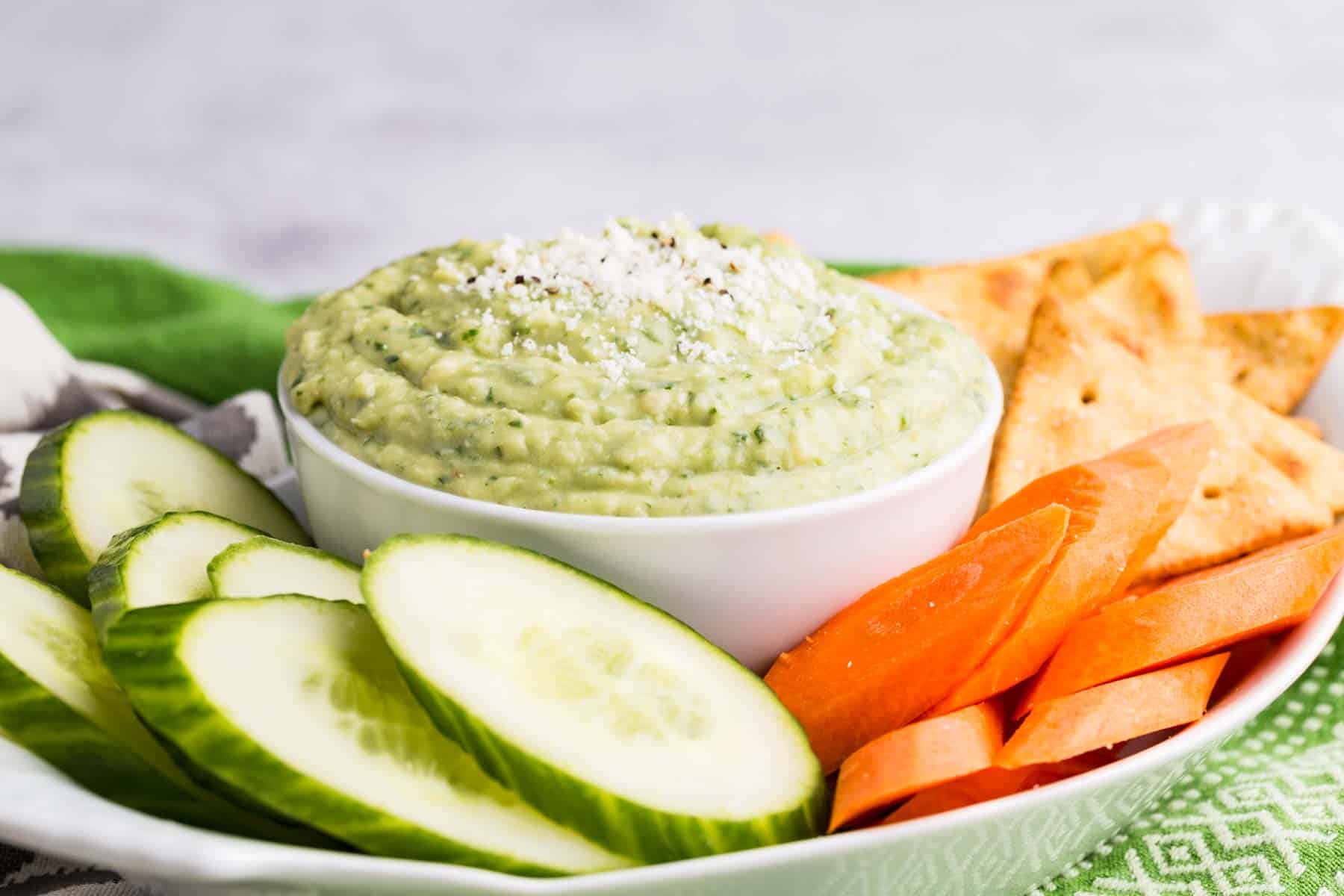 A tray with fresh vegetables and a bowl of green parmesan white bean dip.