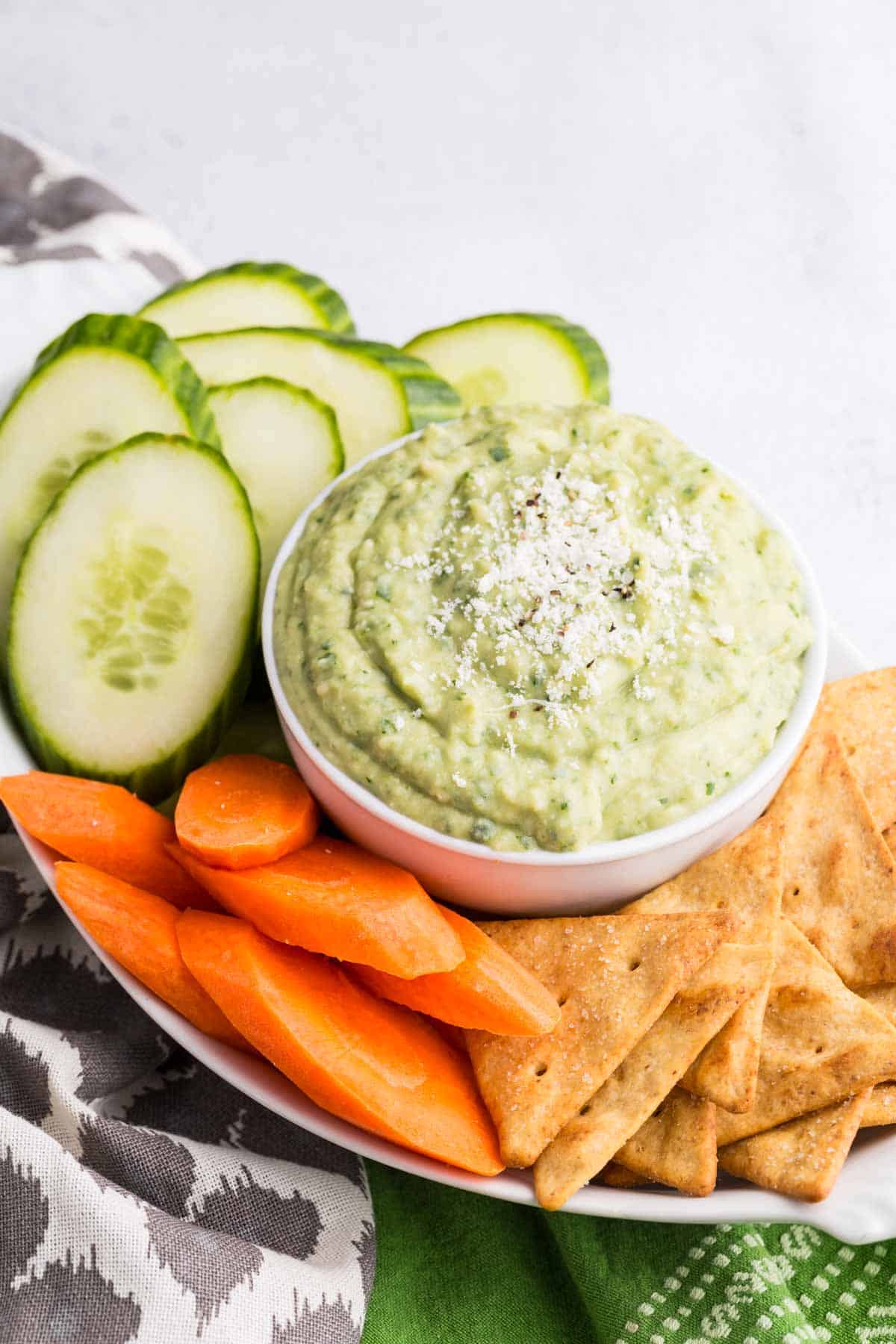 A tray with fresh vegetables and a bowl of green parmesan white bean dip.