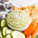 A bowl of parmesan white bean dip with veggies and chips.