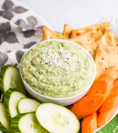 A bowl of parmesan white bean dip with veggies and chips.