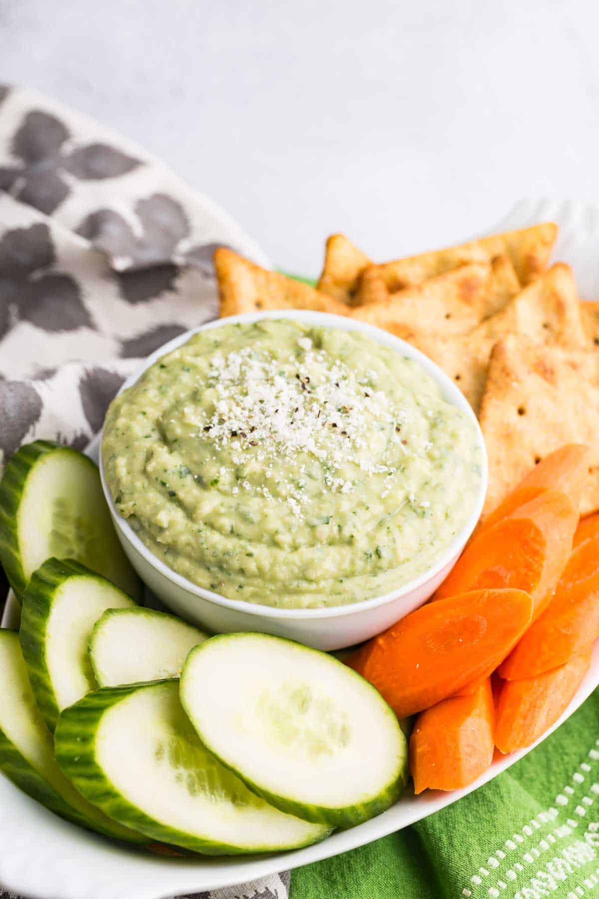 A bowl of parmesan white bean dip with veggies and chips.