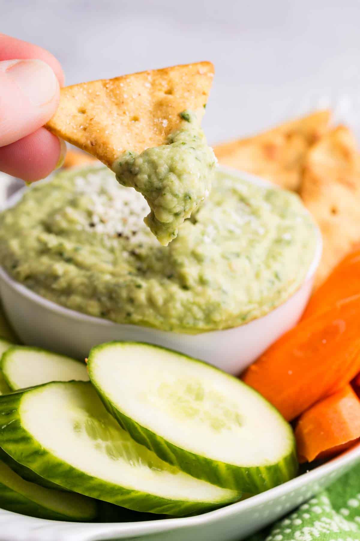 Parmesan white bean dip drips off of a corn chip.