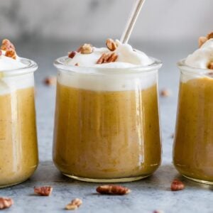 Glasses of pumpkin pudding topped with whipped cream and nuts.