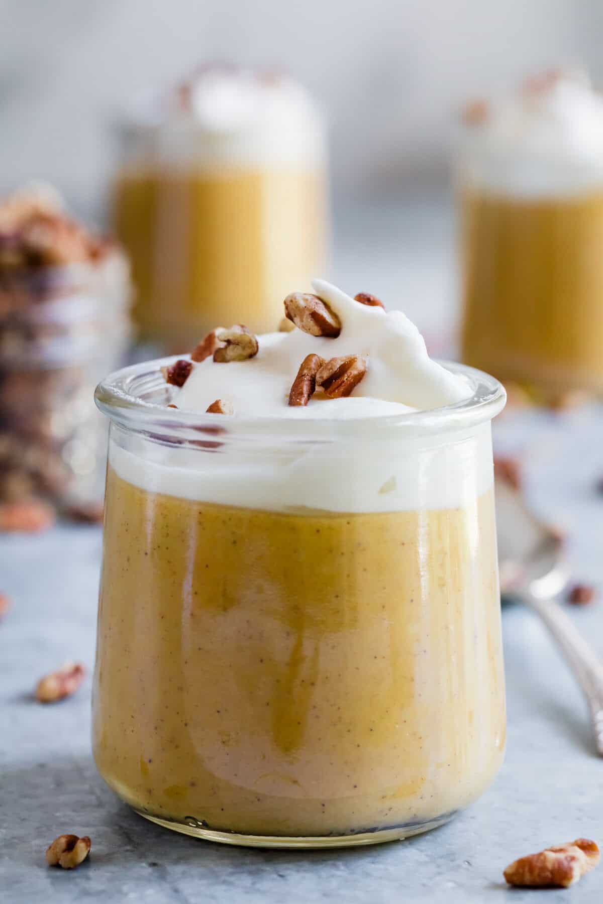 Nuts and whipped cream finish a serving of pumpkin pudding in a glass.