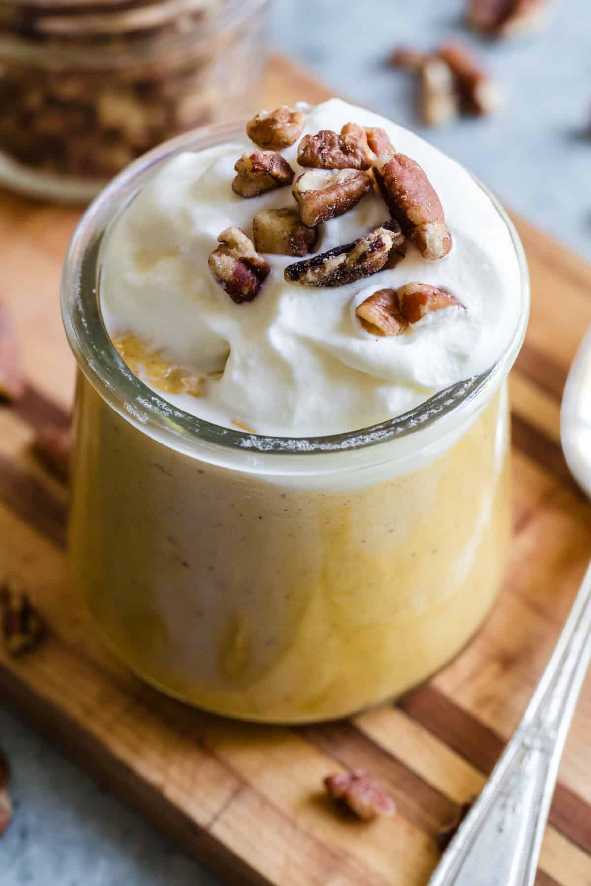 Whipped cream and nuts top a glass of pumpkin pudding.