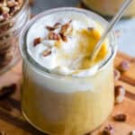 A spoon inserted into a glass jar of pumpkin pudding.