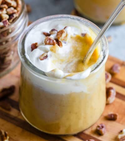 A spoon inserted into a glass jar of pumpkin pudding.